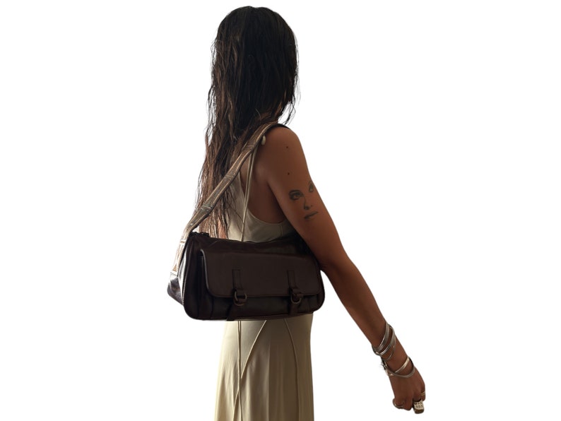 Pu&ograve; includere: Una borsa a tracolla in pelle marrone con una tracolla. La borsa ha due fibbie e una chiusura a lembo.