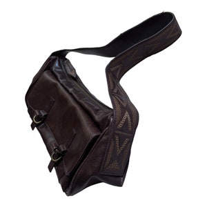 Pu&ograve; includere: Una borsa a tracolla in pelle marrone con una tracolla decorativa con un motivo geometrico. La borsa ha due fibbie sul davanti.
