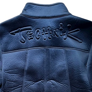 May include: A dark blue jacket with a black embroidered logo that says "Technik" on the back.