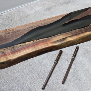 May include: A long, wooden board with a dark green epoxy river running through it. The board has a natural wood grain and a reddish-brown colour. Two brown metal screws are lying on a grey surface below the board.