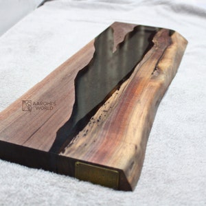 May include: A large wooden serving board with a black epoxy resin inlay. The board has a natural wood grain and a live edge. The board is signed "Aarohi's World".
