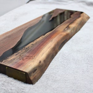 May include: A long, rectangular wooden serving board with a black epoxy resin inlay. The board has a natural wood finish and a live edge. The board is approximately 45 cm long and 15 cm wide. The board is made of walnut wood and has a natural wood grain. The board is perfect for serving cheese, charcuterie, or other appetizers.