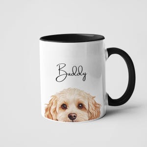 Könnte beinhalten: Weißer Keramikbecher mit schwarzem Innenraum und Griff. Der Becher zeigt eine Aquarellillustration des Gesichts eines Hundes und den Namen "Buddy" in Schreibschrift. Der Hund hat hellbraunes Fell und braune Augen.