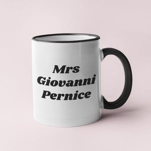 Op de afbeelding: Witte keramische mok met een zwarte rand en handvat. De mok heeft de tekst "Mrs Giovanni Pernice" in zwart gedrukt.