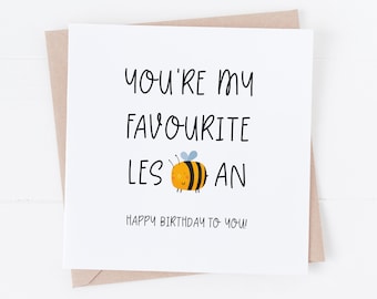 May include: A white greeting card with the text "You're my favourite lesbian" and a cartoon bee illustration. The card also includes the phrase "Happy Birthday to you!" and is placed on a brown envelope.