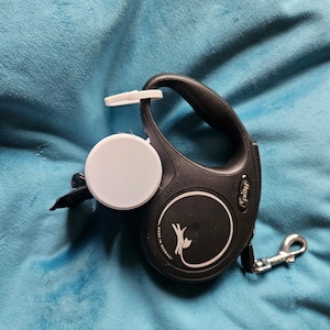 May include: A black retractable dog lead with a white logo and the word "flexi" printed on it. The lead is made in Germany and has a white plastic handle.