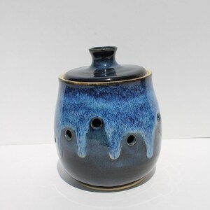 May include: A ceramic garlic keeper with a dark blue lid and a body that transitions from a lighter blue to a deep navy. The jar has several circular holes near the top. A functional and decorative kitchen item.