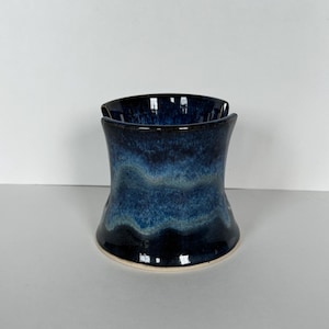 May include: A handmade ceramic vase with a unique, flared shape. The vase features a gradient of deep blues, transitioning from a dark base to lighter shades towards the middle. The rim is dark blue, and the base is a light beige.