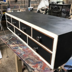May include: Black wooden drawer unit with six drawers and white trim. Each drawer has a silver knob.