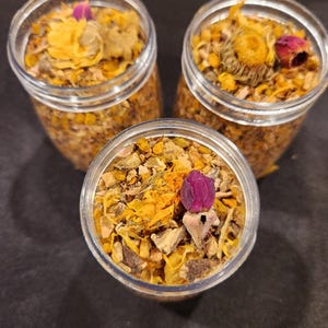 Puede incluir: Tres frascos de vidrio llenos de una mezcla de hierbas, flores y especias secas. Los frascos est&aacute;n llenos de una mezcla de ingredientes secos amarillos, naranjas y morados.