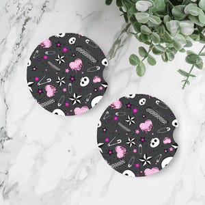 Puede incluir: Dos posavasos redondos para coche con fondo gris oscuro y un estampado de calaveras blancas, corazones rosas, estrellas, imperdibles y patrones de cuadros. Los posavasos están diseñados para encajar en el portavasos del coche.