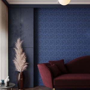 May include: A burgundy velvet sofa with gold legs sits in a room with a blue patterned wall and a tall vase with dried pampas grass.