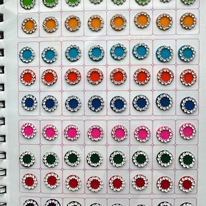 May include: A sheet of colorful round stickers with a silver trim. The stickers are arranged in rows and columns. The colors include red, orange, yellow, blue, green, pink, purple, and black. The text "Raavya Kumkum Bindi" is printed at the top of the sheet.