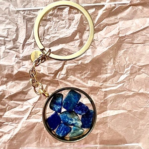 May include: A gold keychain with a clear round charm containing blue lapis lazuli stones.