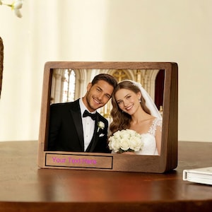 May include: A wooden picture frame with a wedding photo of a smiling couple. The frame has a rectangular shape with rounded corners and a small rectangular space at the bottom that says "Your Text Here".