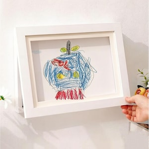 Op de afbeelding: Witgelijst kunstwerk met een kindertekening. De tekening is een kleurrijk, abstract ontwerp met blauwe, rode, gele en groene kleurpotloodstreken. De vierkante lijst heeft een strakke, moderne uitstraling, ideaal voor kinderkunst.