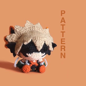 May include: Crocheted plush toy of a character with spiky orange and brown hair, black eyes, and a white face. The toy is wearing a green, orange, and black outfit.