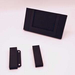 May include: A black picture frame with two black stand pieces. The frame has a rectangular opening for a photo.