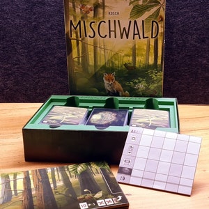 Könnte beinhalten: Eine grüne Box mit den Worten "Mischwald" und "Kosch" auf der Vorderseite. Die Box enthält ein Spiel mit Karten und einem Punkteblatt. Das Spiel spielt in einem Wald mit einem Fuchs und einem Schmetterling.