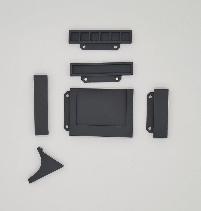 May include: A set of six black plastic pieces for a craft project. The pieces include a rectangular frame, a smaller rectangular frame, a long thin rectangle, a short thin rectangle, and two L-shaped pieces.