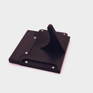 May include: A black plastic stand with a raised, angled platform. The stand has several small, round, silver-colored dots on the surface.