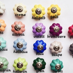 Könnte beinhalten: Eine Sammlung von 12 Keramik-Knöpfen in verschiedenen Farben, darunter Weiß, Creme, Gelb, Orange, Rosa, Lila, Blau, Grün, Grau und Türkis. Jeder Knopf hat einen gewellten Rand und eine silberne Metallmitte.