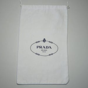 Peut inclure: Un sac de protection en tissu blanc avec un cordon de serrage, arborant le logo bleu foncé Prada Milano dal 1913 centré sur le devant. Cette pochette rectangulaire possède une fermeture simple avec des cordons blancs sur le dessus.