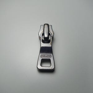 Cremallera de repuesto Coach plateada con relieve metálico