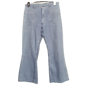 May include: Light blue denim pants featuring a high-waisted design with a button and zipper fly closure, belt loops, and two large square patch pockets on the front. The legs have a flared silhouette that widens toward the bottom hem.