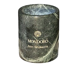 May include: A cylindrical dark green marble wine cooler with white veining. The front features a gold-colored emblem above the text MONDORO and ASTI SPUMANTE printed in gold lettering. The interior is hollow with a smooth, polished stone finish.