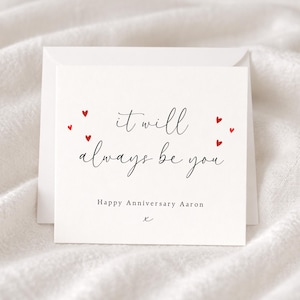 May include: A white square anniversary card with the message "it will always be you" in black script, decorated with red heart shapes. The card also includes the text "Happy Anniversary Aaron" and a small "x".