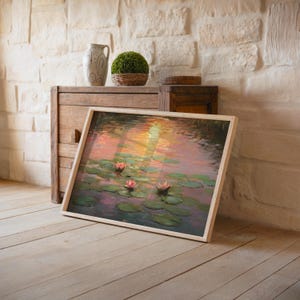 May include: A framed art print of water lilies in a pond, featuring pink and white flowers and green lily pads. The artwork has a light wood frame and is propped against a wooden cabinet. A decorative vase and topiary are also visible.