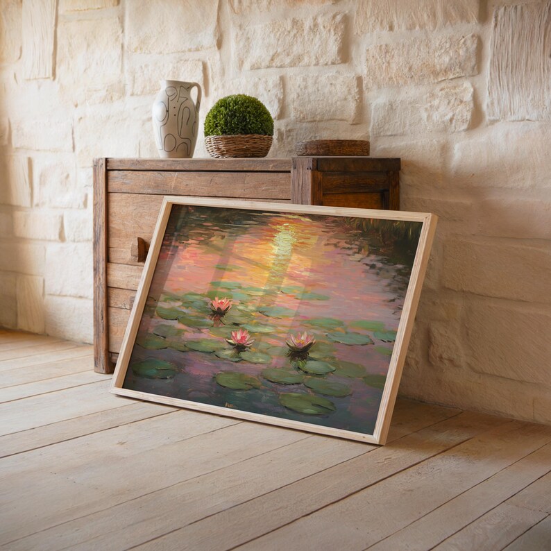 May include: A framed art print of water lilies in a pond, featuring pink and white flowers and green lily pads. The artwork has a light wood frame and is propped against a wooden cabinet. A decorative vase and topiary are also visible.