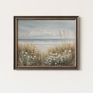Puede incluir: Pintura enmarcada de un paisaje costero. La obra presenta hierbas doradas y flores silvestres blancas en primer plano, que conducen a una playa de arena y al mar bajo un cielo nublado. El marco es oscuro con detalles dorados.