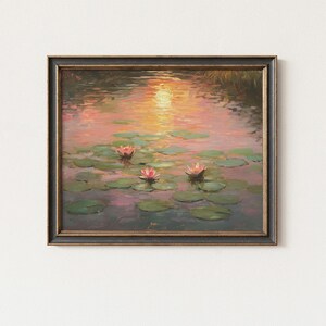 May include: Framed painting depicting a tranquil water scene with lily pads and pink water lilies. The sunset reflects on the water, creating a warm atmosphere. The frame is dark with gold detailing.