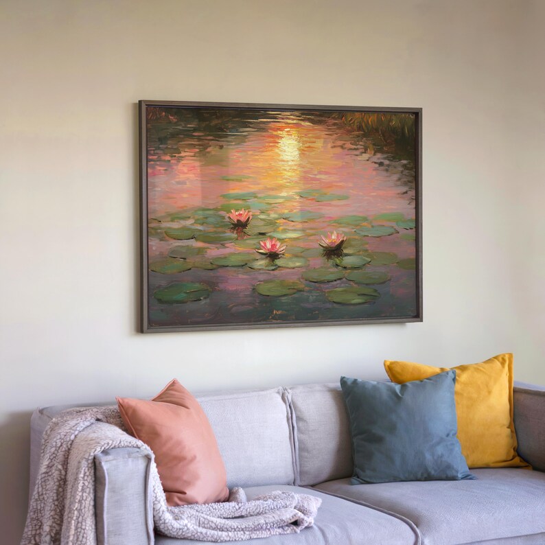 May include: A framed painting of a water scene with lily pads and pink water lilies. The artwork features a sunset with warm orange and pink hues reflected in the water. The painting is displayed above a grey sofa with colourful cushions.