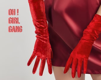 Può includere: Un paio di lunghi guanti di velluto rosso. I guanti sono indossati da una persona che indossa un vestito rosso. Il testo "OH! GIRL GANG" è visibile nell'immagine.