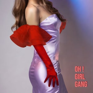 Op de afbeelding: Een vrouw draagt een strapless, lavendelkleurige satijnen jurk met een rode gerimpelde schouderloze mouw en bijpassende rode satijnen handschoenen. De tekst "OH! GIRL GANG" is in roze op een witte achtergrond gedrukt.