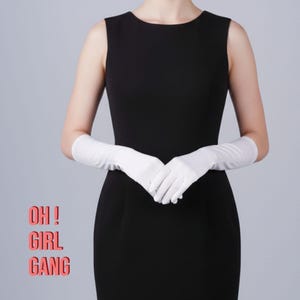Könnte beinhalten: Ein ärmelloses schwarzes Kleid, kombiniert mit langen weißen Handschuhen. Die Handschuhe reichen über die Ellbogen hinaus. Der Text "OH! GIRL GANG" wird in einem rosa Rechteck unten links angezeigt.