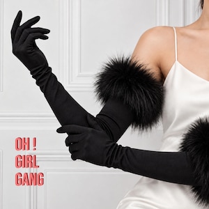 May include: Long black opera-length gloves featuring a thick band of black faux fur trim at the upper arm. The text "OH ! GIRL GANG" is printed in red on the left side. The gloves are made of a smooth, matte fabric and extend past the elbow.