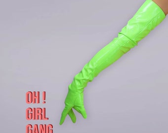 Könnte beinhalten: Ein langer, leuchtend neongrüner Opernhandschuh mit glänzender, lackartiger Oberfläche, der bis über den Ellbogen reicht. Der Text "OH ! GIRL GANG" ist in einer fetten, lachsrosa serifenlosen Schrift links vom Handschuh auf hellgrauem Grund.
