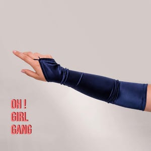 May include: Navy blue arm warmers with a finger loop. The arm warmers are made of a soft, shiny material. The text "OH! GIRL GANG" is printed in pink.