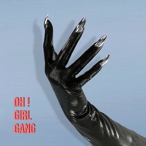 May include: A black glove with long, silver metallic fingernails. The text "OH! GIRL GANG" is displayed in red. The glove is shiny and appears to be made of a leather-like material, set against a light blue background.