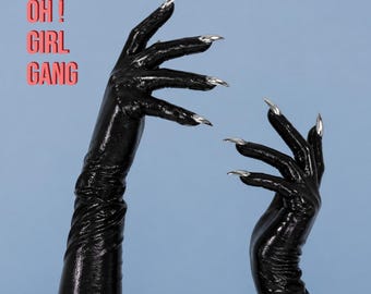 May include: A pair of long, black, glossy, wet-look gloves with sharp, metallic silver claw-like fingernail attachments. The text "OH! GIRL GANG" is printed in red on the left side. The gloves extend past the wrists.