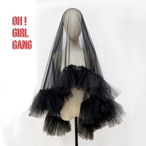 Puede incluir: Velo de tul negro con un dise&ntilde;o de volantes en capas. El velo se exhibe en un maniqu&iacute; y presenta el texto "OH! GIRL GANG" en rosa. Un accesorio dram&aacute;tico.