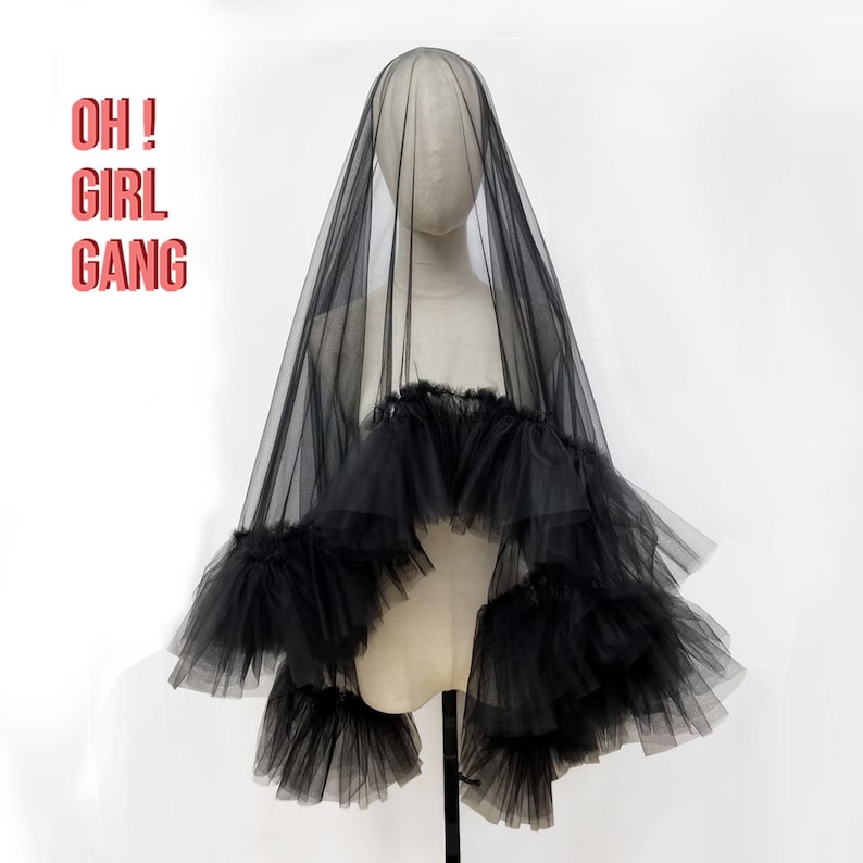 Puede incluir: Velo de tul negro con un dise&ntilde;o de volantes en capas. El velo se exhibe en un maniqu&iacute; y presenta el texto "OH! GIRL GANG" en rosa. Un accesorio dram&aacute;tico.