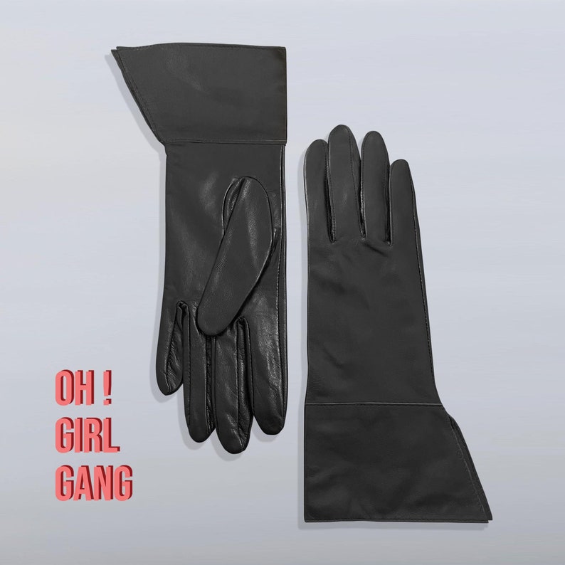 Pode incluir: Um par de luvas de couro preto. Uma luva &eacute; longa, sem dedos e com punho. A outra luva &eacute; uma luva completa com dedos. O texto "OH! GIRL GANG" est&aacute; impresso em um fundo branco.