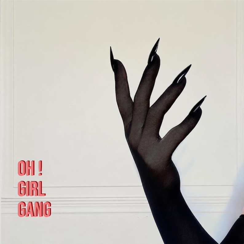 May include: A pair of sheer black opera-length gloves featuring long, pointed, claw-like fingertips. The text "OH ! GIRL GANG" is printed in a bold, red, sans-serif font on the left side of the frame against a plain, light-colored background.