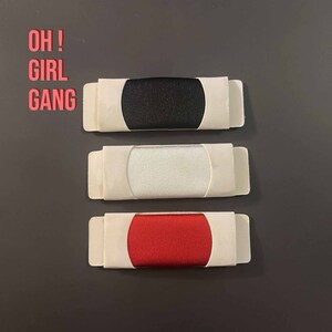 May include: Three fabric swatches in white, black, and red, each displayed in a white cardboard frame. The text "OH! GIRL GANG" is written in red above the swatches.