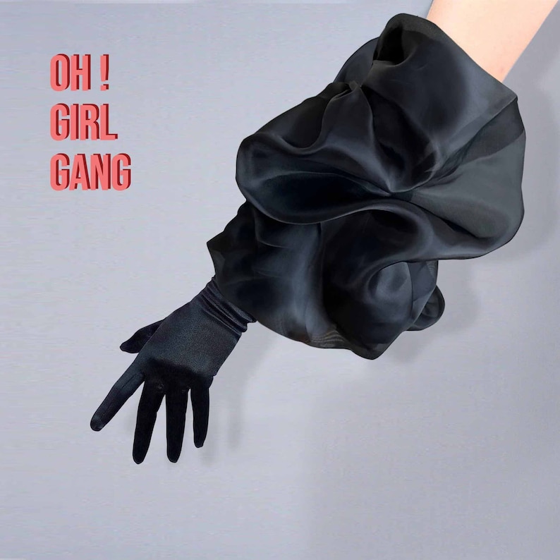 May include: A black satin glove with a large, puffy black sleeve. The text "OH! GIRL GANG" is written in pink letters on a white background.